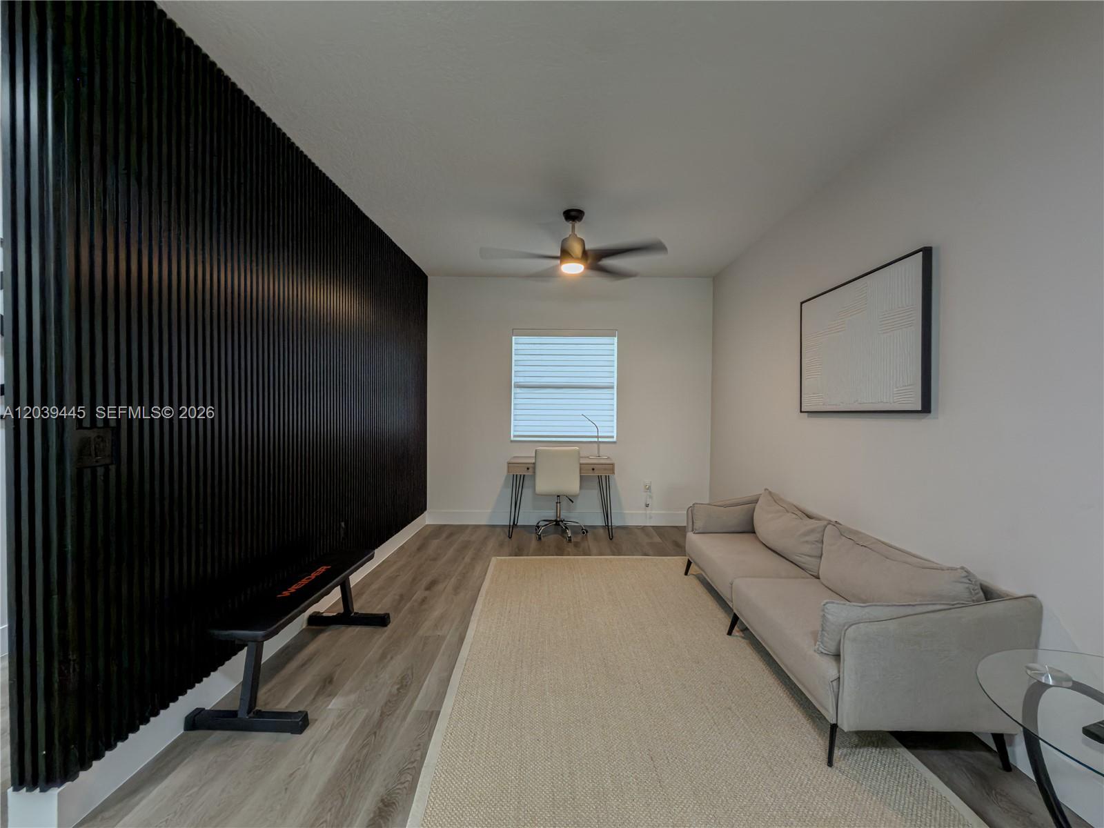 A room features a black slatted accent wall, a gray sofa, and a small desk — 10750 NW 66th St # 504, Doral FL 33178, DORAL, FL