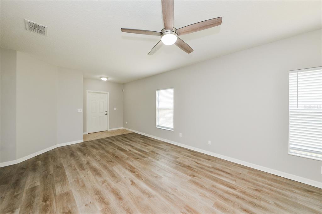 An empty living room features light gray walls, wood-look flooring, a ceiling fan, and two windows — 2114 RICHWOOD PIKE DRIVE, RUSKIN, FL