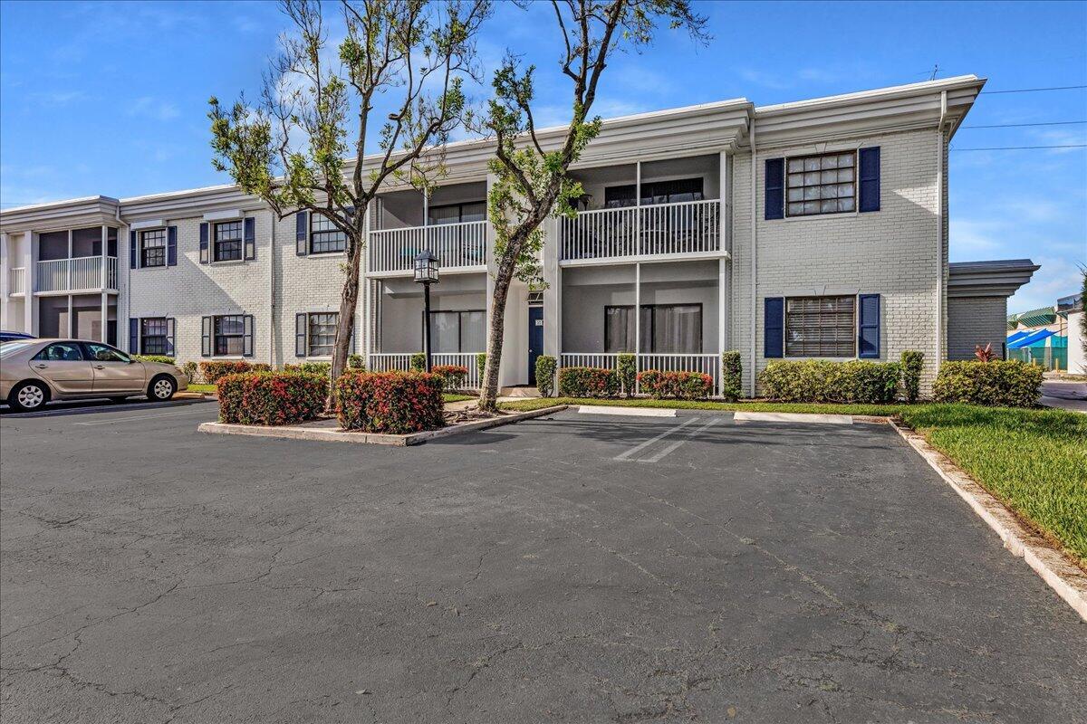 A two-story apartment building with white brick siding, blue shutters, and a paved parking lot — 180 Cypress Club Drive # 816, Pompano Beach FL 33060, POMPANO BEACH, FL