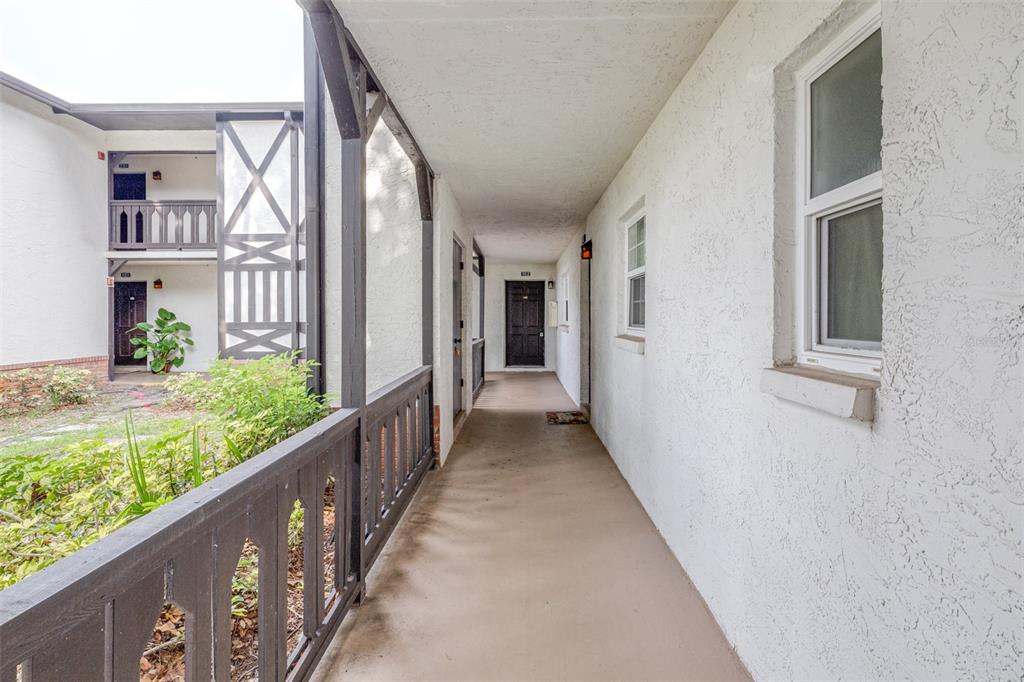 An outdoor walkway with a dark wooden railing leads to a dark brown apartment door — 420 N BAYSHORE BOULEVARD UNIT 102, CLEARWATER, FL