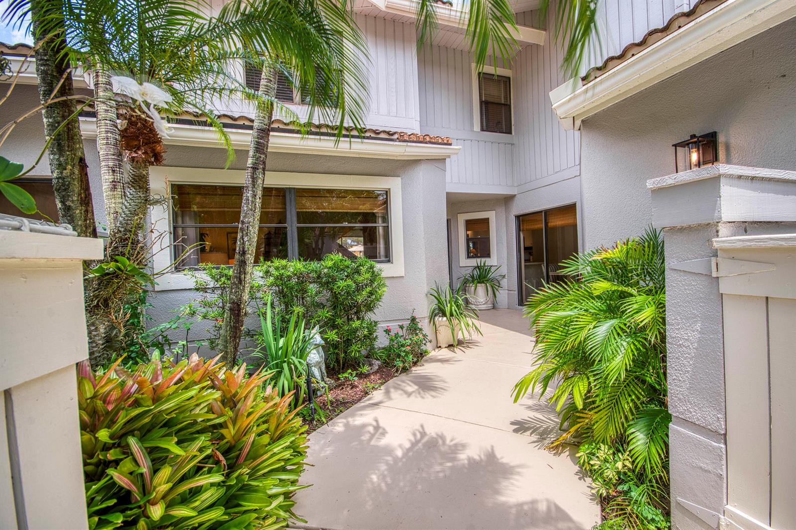 A concrete walkway leads to the entrance of a two-story house with tropical landscaping — 525 Prestwick Circle, Palm Beach Gardens FL 33418, PALM BEACH GARDENS, FL