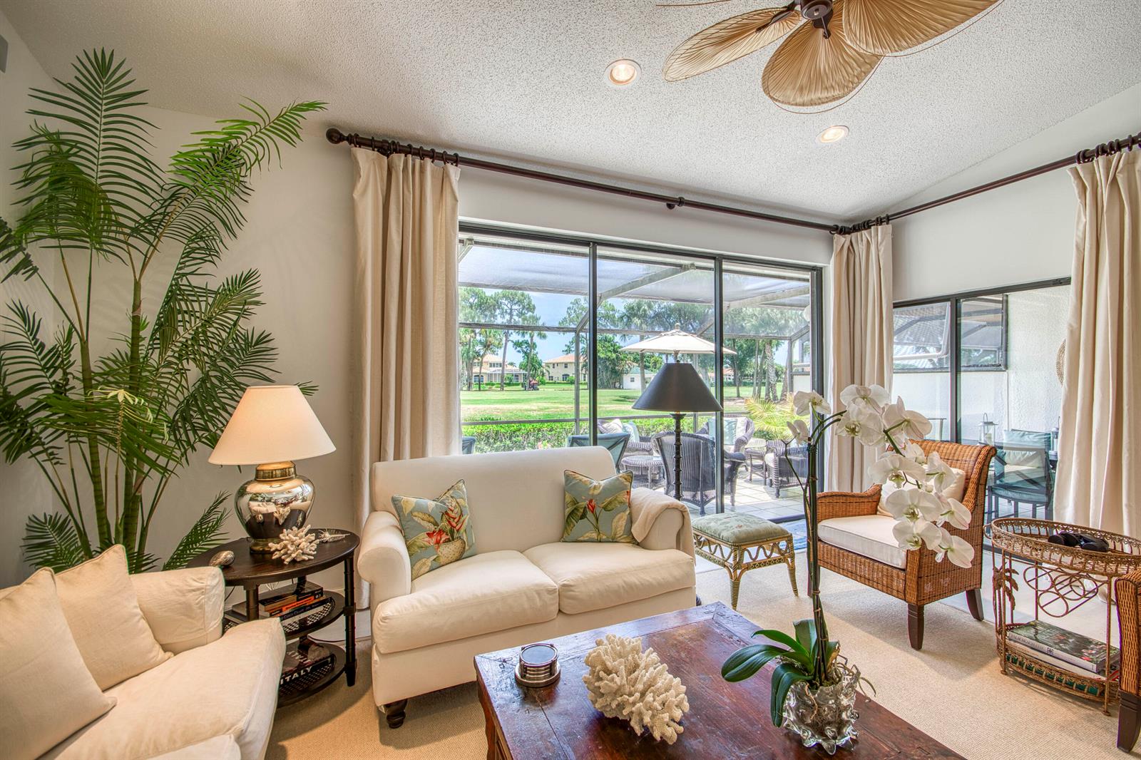 A bright living room features white furniture, a wooden coffee table, and sliding glass doors — 525 Prestwick Circle, Palm Beach Gardens FL 33418, PALM BEACH GARDENS, FL