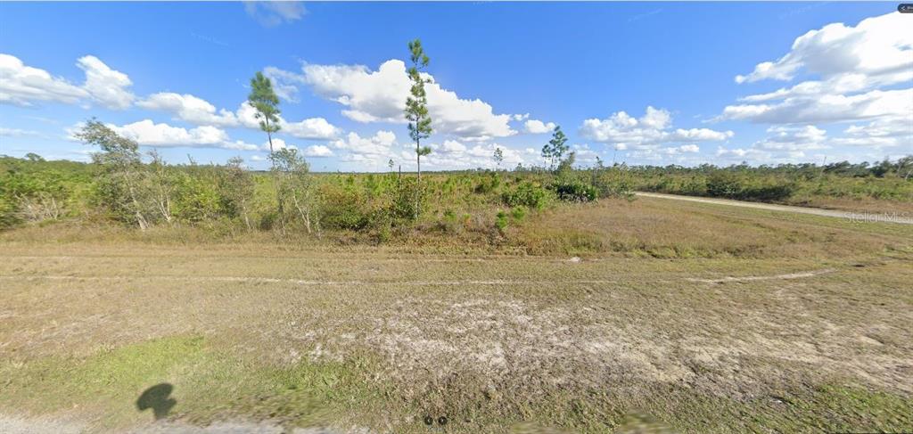 A vacant, grassy lot features scattered trees and shrubs under a bright, partly cloudy sky — 724 ALTHEA DRIVE, INDIAN LAKE ESTATES, FL