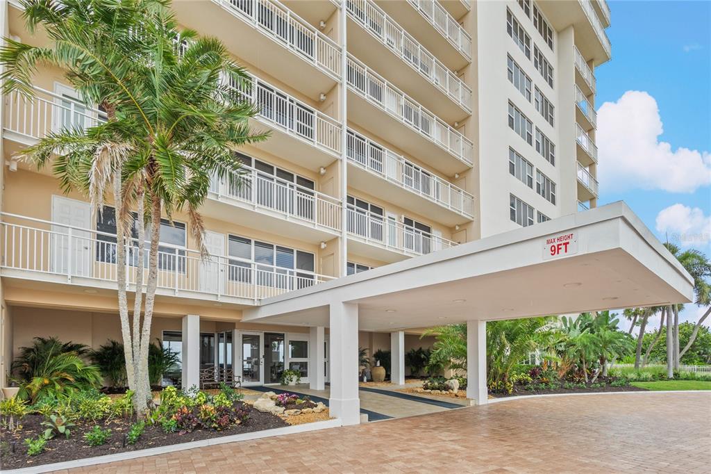 The exterior of a multi-story apartment building features a covered entrance with a palm tree — 603 LONGBOAT CLUB ROAD UNIT 202N, LONGBOAT KEY, FL