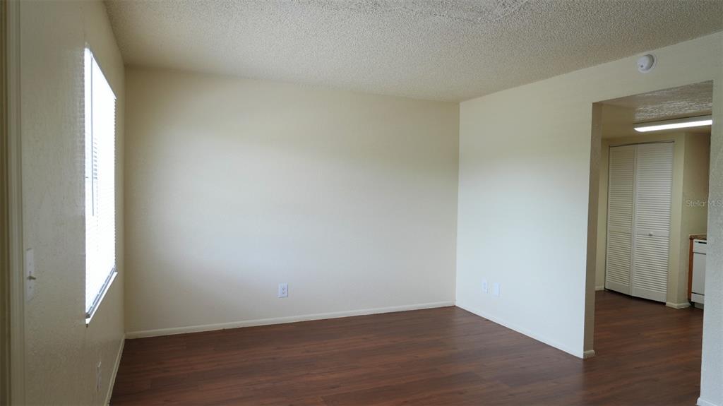 An empty room with wood-look flooring, beige walls, and a doorway leading to a kitchen — 4015 76TH AVENUE N UNIT 4025, PINELLAS PARK, FL