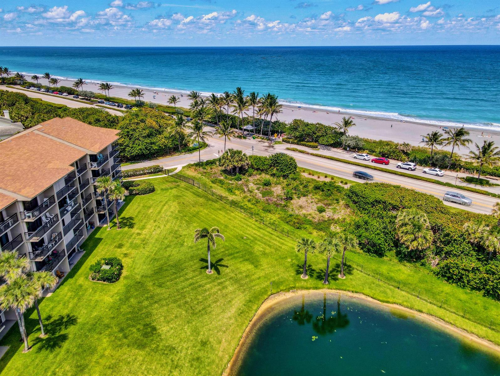 An aerial view shows a multi-story apartment building, a grassy lawn, a pond, and beach — 201 S Seas Drive # 401, Jupiter FL 33477, JUPITER, FL