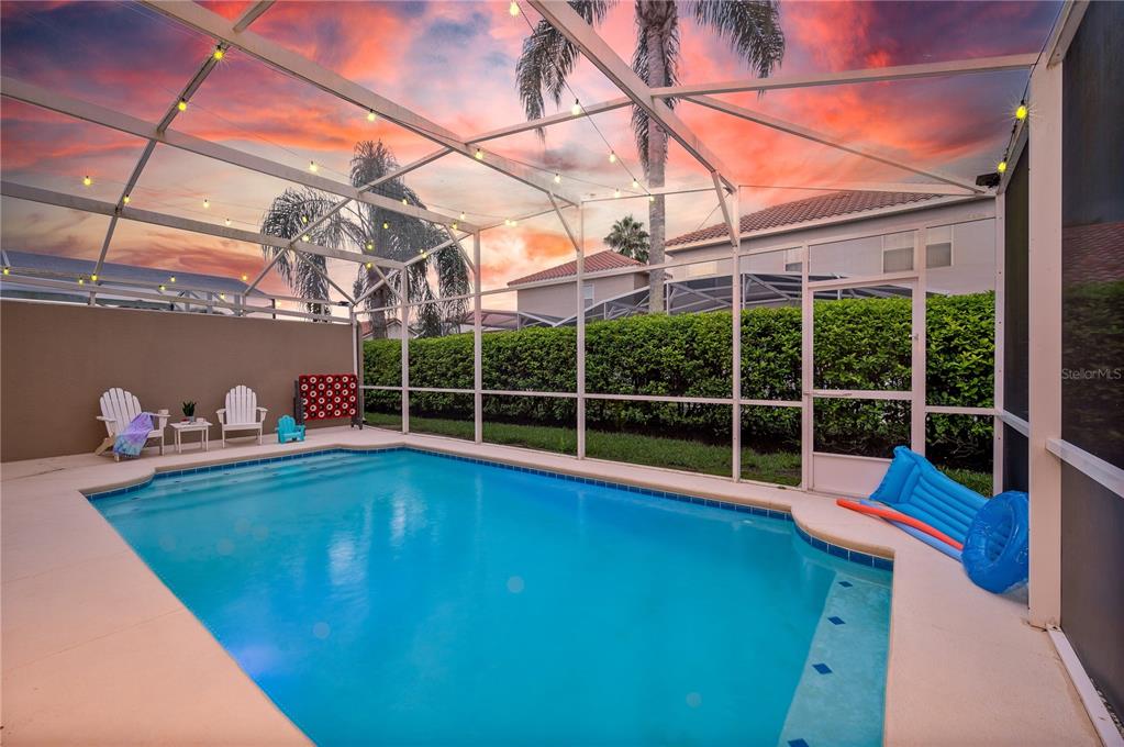 A swimming pool with a screened-in enclosure and patio furniture at sunset — 740 BRUNELLO DRIVE, DAVENPORT, FL