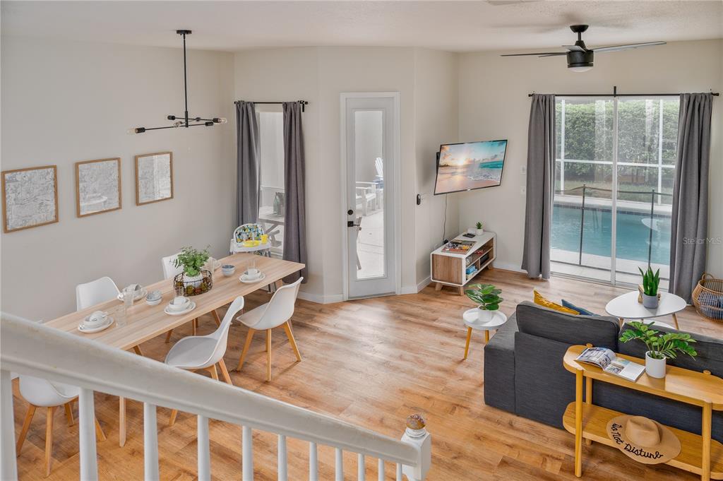 An open-concept living and dining area features wood-look flooring, a pool view, and stairs — 740 BRUNELLO DRIVE, DAVENPORT, FL