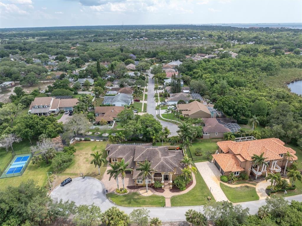 An aerial view shows a large suburban neighborhood with houses, a tennis court, and trees — 1067 ASHLAND AVENUE, TARPON SPRINGS, FL