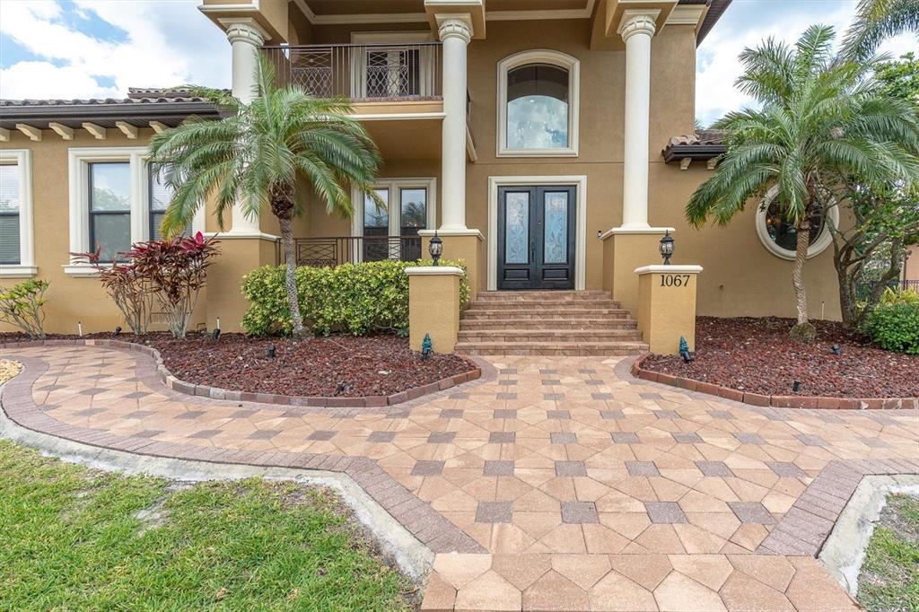 A two-story house exterior features a paved walkway, palm trees, and a double front door — 1067 ASHLAND AVENUE, TARPON SPRINGS, FL
