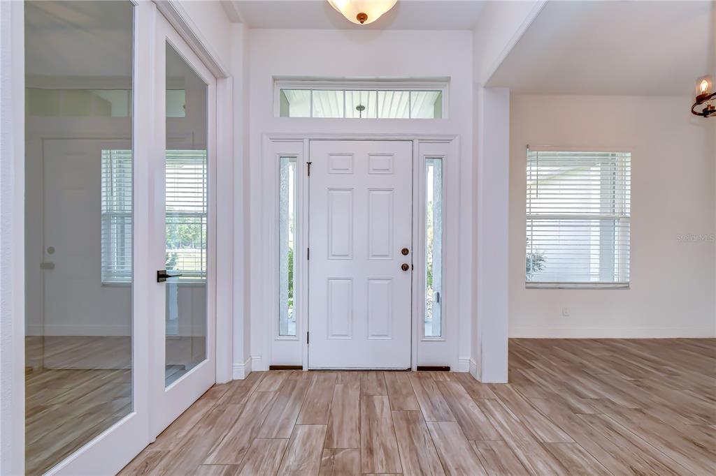 A bright entryway features a white front door with sidelights, wood-look flooring, and glass-paneled doors — 4008 MCINTOSH ESTATES LANE, PLANT CITY, FL