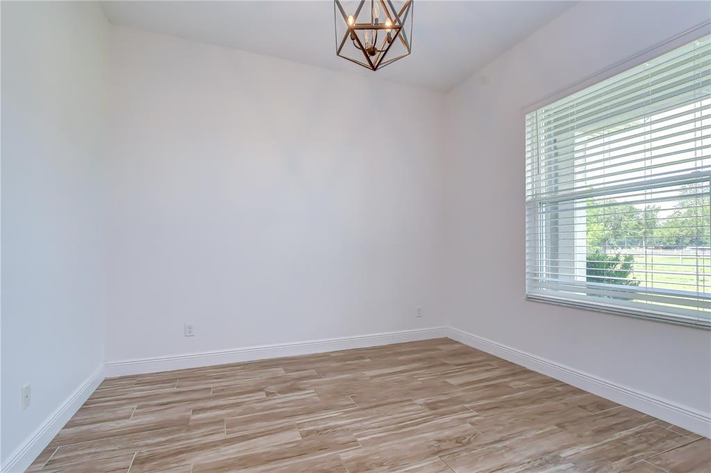 An empty room features white walls, wood-look tile flooring, a geometric chandelier, and a large window — 4008 MCINTOSH ESTATES LANE, PLANT CITY, FL