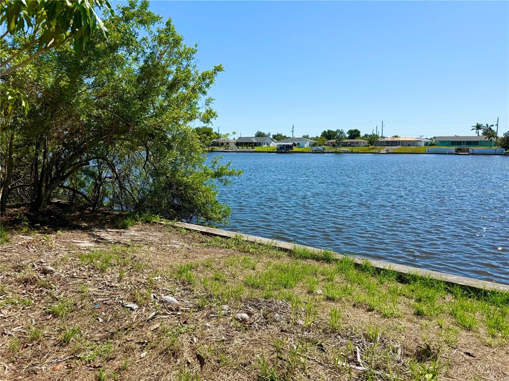 A view of a canal from a grassy, tree-lined waterfront lot — 834 ELLICOTT CIRCLE NW, PORT CHARLOTTE, FL