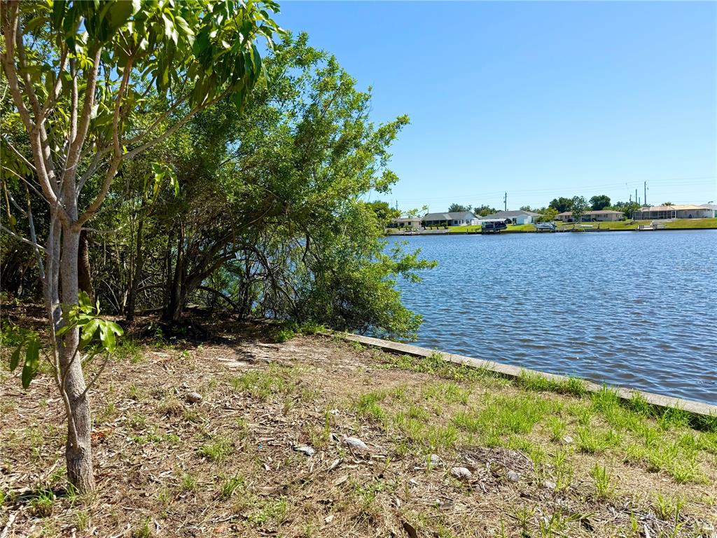 A view of a grassy waterfront lot with trees and houses across the canal — 834 ELLICOTT CIRCLE NW, PORT CHARLOTTE, FL