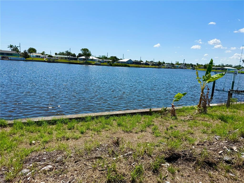 A view of a canal from a grassy backyard with a concrete seawall — 834 ELLICOTT CIRCLE NW, PORT CHARLOTTE, FL