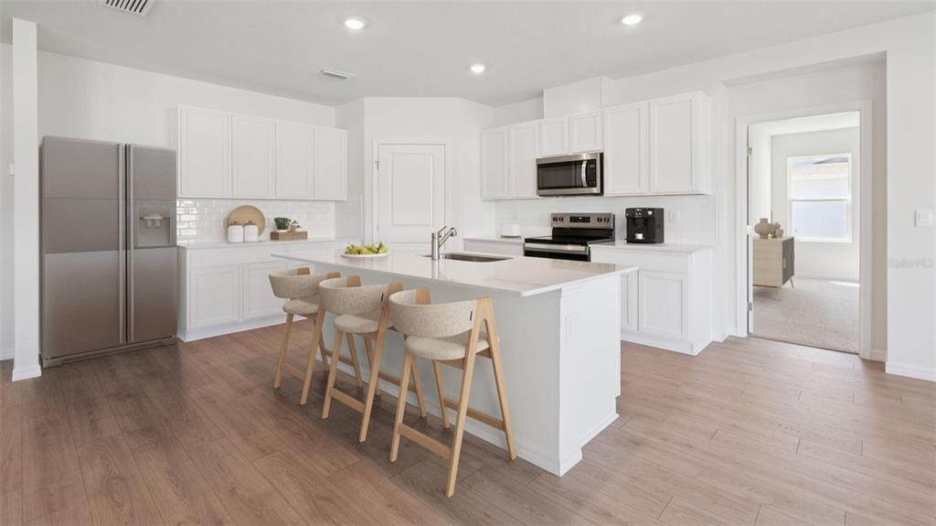 A modern kitchen features white cabinetry, a central island with bar stools, and wood flooring — 24226 NW 13TH BOULEVARD, NEWBERRY, FL