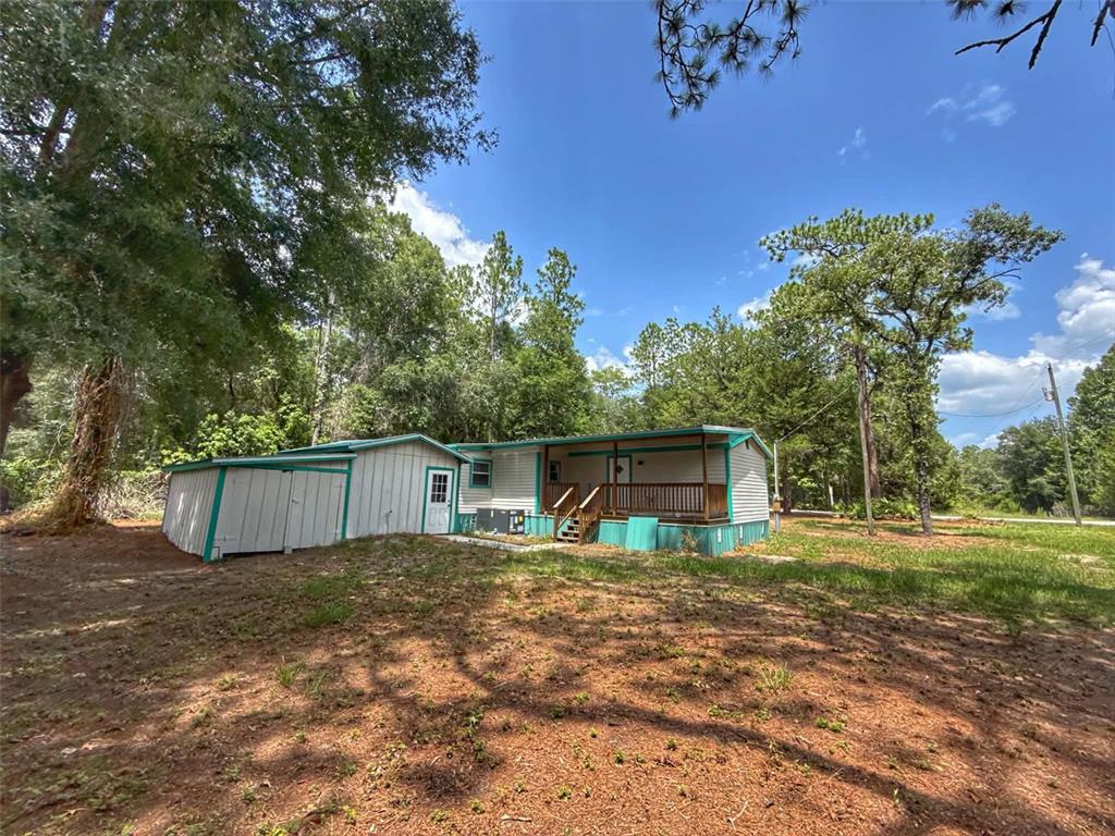 A mobile home with a wooden deck and an attached shed sits in a wooded lot — 65 NE 528TH AVENUE, OLD TOWN, FL