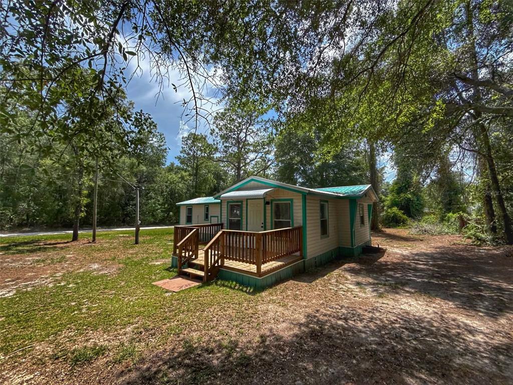 A small, tan-sided house with a green metal roof and a wooden front deck — 65 NE 528TH AVENUE, OLD TOWN, FL