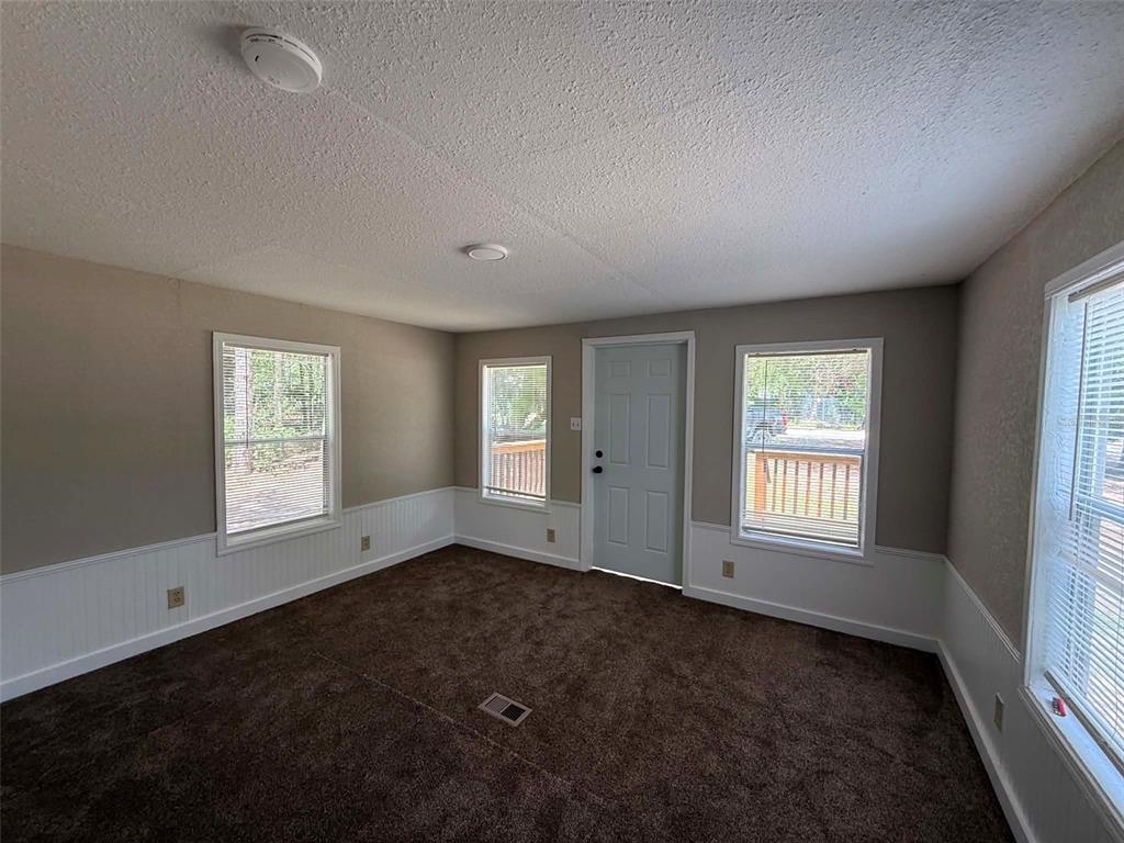 A room with brown carpet, white wainscoting, three windows, and a light-colored entry door — 65 NE 528TH AVENUE, OLD TOWN, FL
