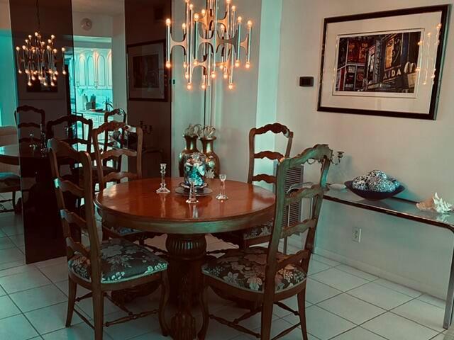 A dining room features a round wooden table, patterned chairs, and a modern chandelier — 101 Briny Avenue # 707, Pompano Beach FL 33062, POMPANO BEACH, FL