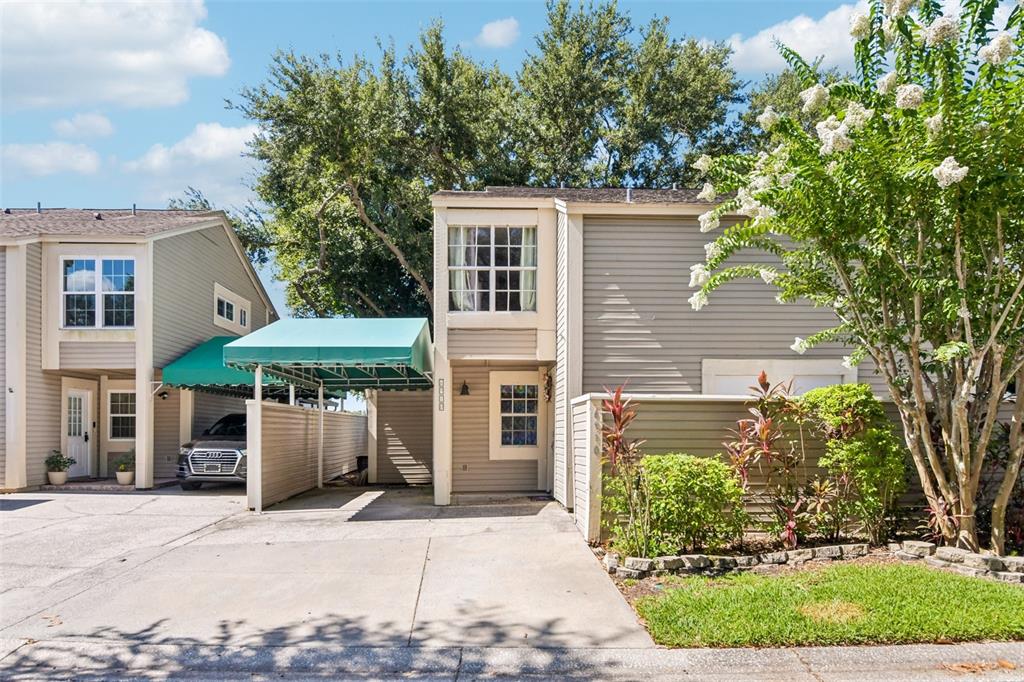 A two-story tan townhouse with a green carport and a small front garden — 6910 LAKE PLACE COURT, TAMPA, FL