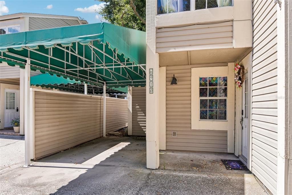 A tan house exterior features a green metal carport, a stained-glass window, and a front door — 6910 LAKE PLACE COURT, TAMPA, FL