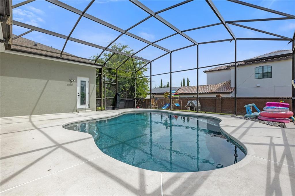 A screened-in patio features a kidney-shaped swimming pool and a concrete deck — 10175 COVE LAKE DRIVE, ORLANDO, FL
