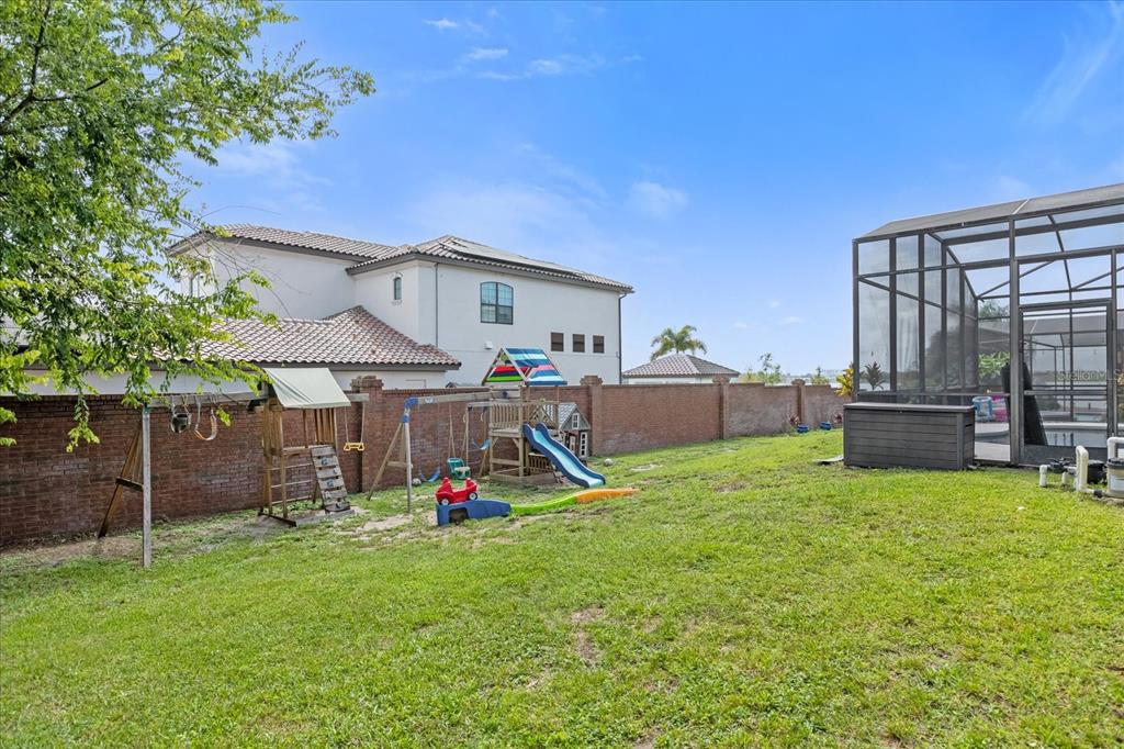 A backyard features a wooden playset, a grassy lawn, and a screened-in pool enclosure — 10175 COVE LAKE DRIVE, ORLANDO, FL