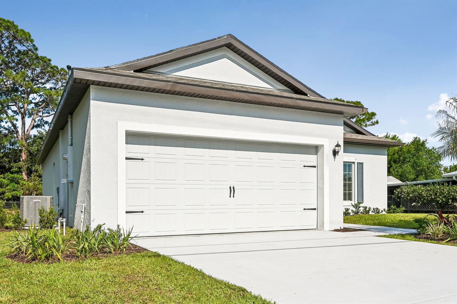 A white stucco house features a two-car garage with decorative hardware and a concrete driveway — 5901 Raintree Trail, Fort Pierce FL 34982, FORT PIERCE, FL