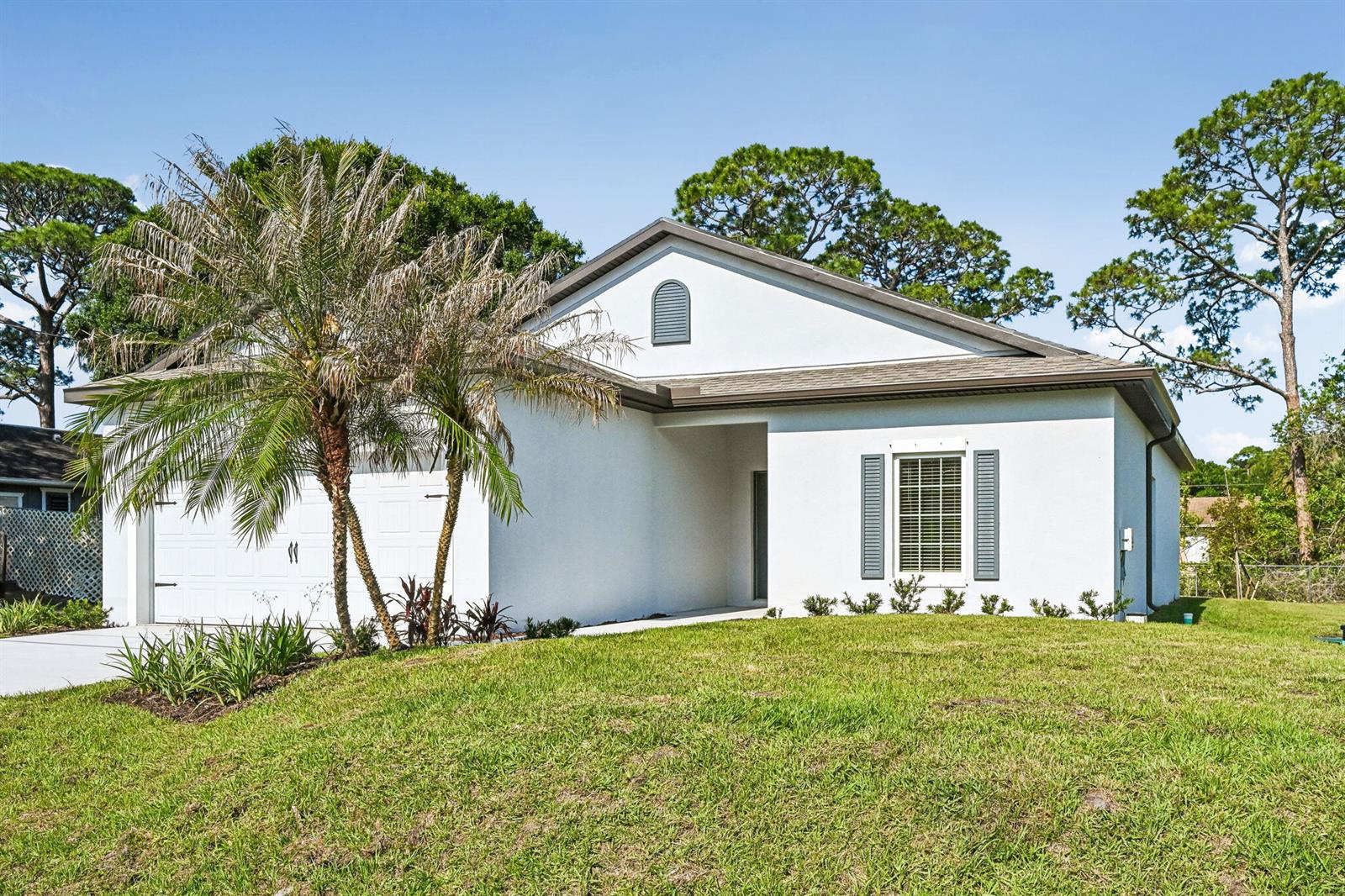 A white single-story house with a two-car garage, gray shutters, and a palm tree — 5901 Raintree Trail, Fort Pierce FL 34982, FORT PIERCE, FL