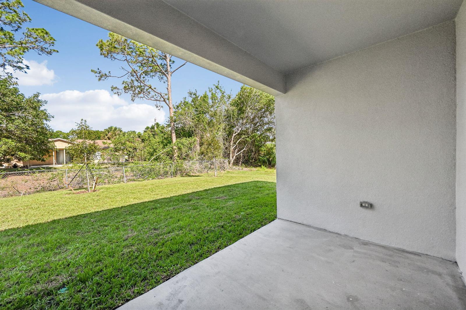 A covered concrete patio overlooks a grassy backyard with trees and a chain-link fence — 5901 Raintree Trail, Fort Pierce FL 34982, FORT PIERCE, FL