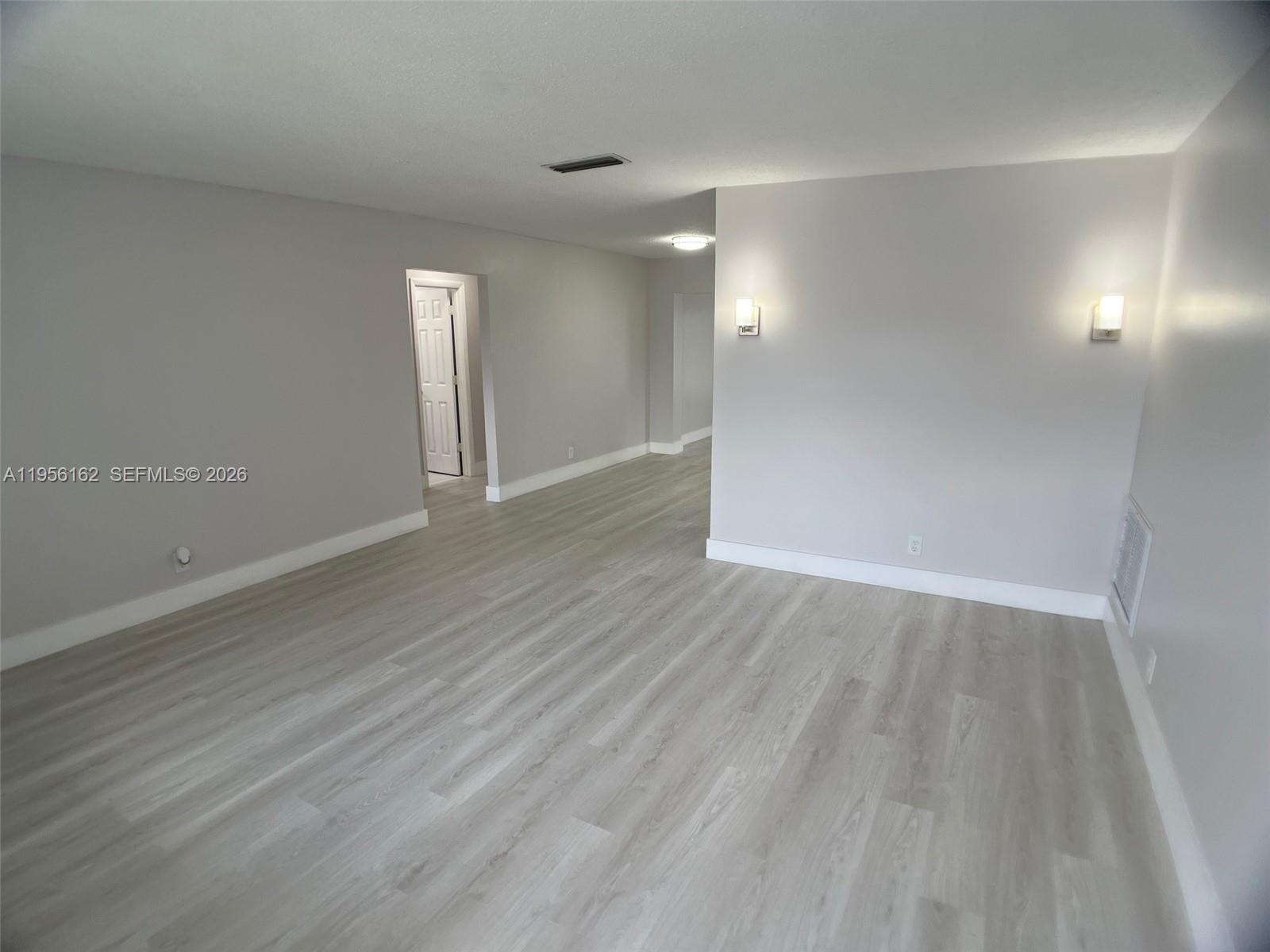 An empty room features light gray walls, wood-look flooring, and two wall-mounted sconces — 6990 NW 17th St, Margate FL 33063, MARGATE, FL