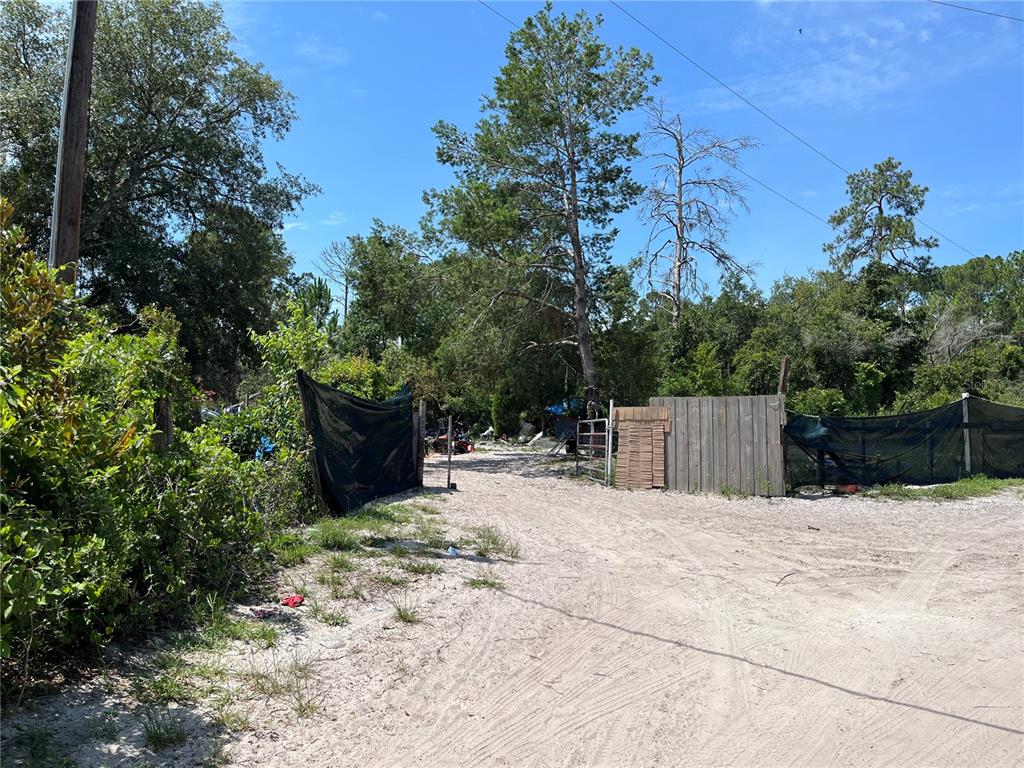 A dirt driveway leads to a gated entrance with wooden fencing and black privacy netting — 42334 W LAKE ROAD, DELAND, FL