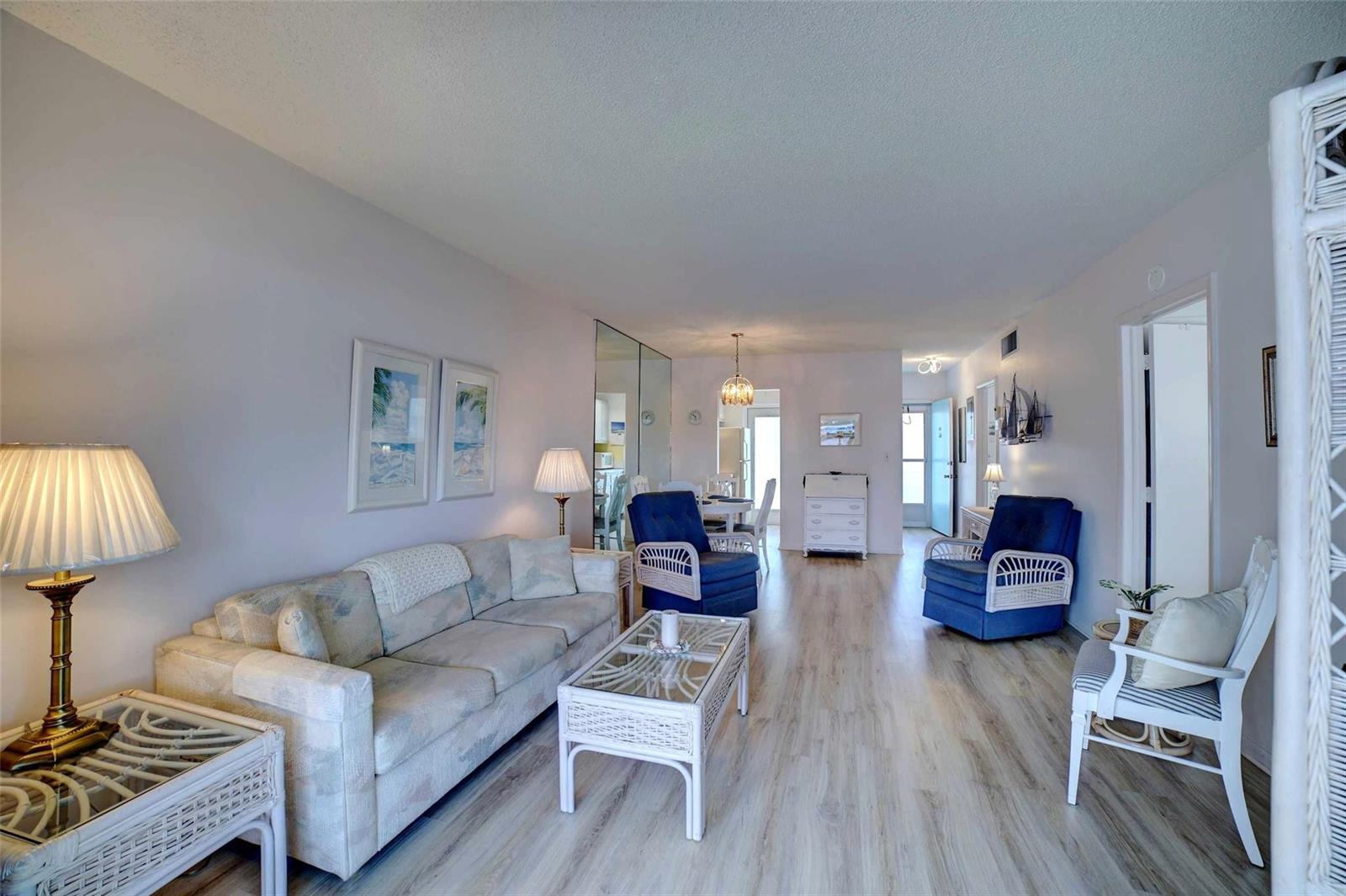 A living room features light wood-look flooring, a patterned sofa, blue armchairs, and wicker furniture — 1801 Ocean Drive # 201, Boynton Beach FL 33426, BOYNTON BEACH, FL