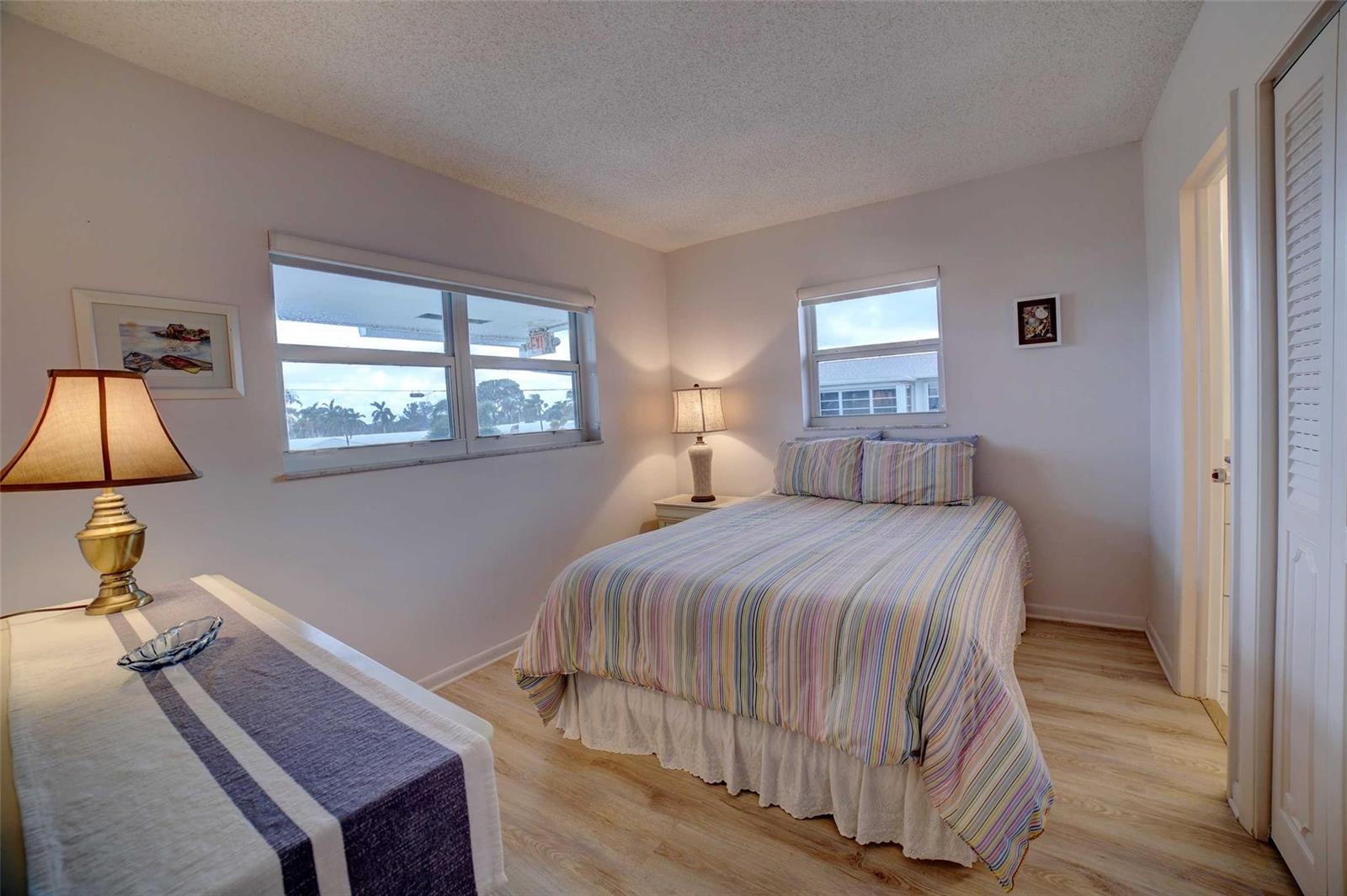 A bedroom with a bed, a dresser, two windows, and light wood-look flooring — 1801 Ocean Drive # 201, Boynton Beach FL 33426, BOYNTON BEACH, FL