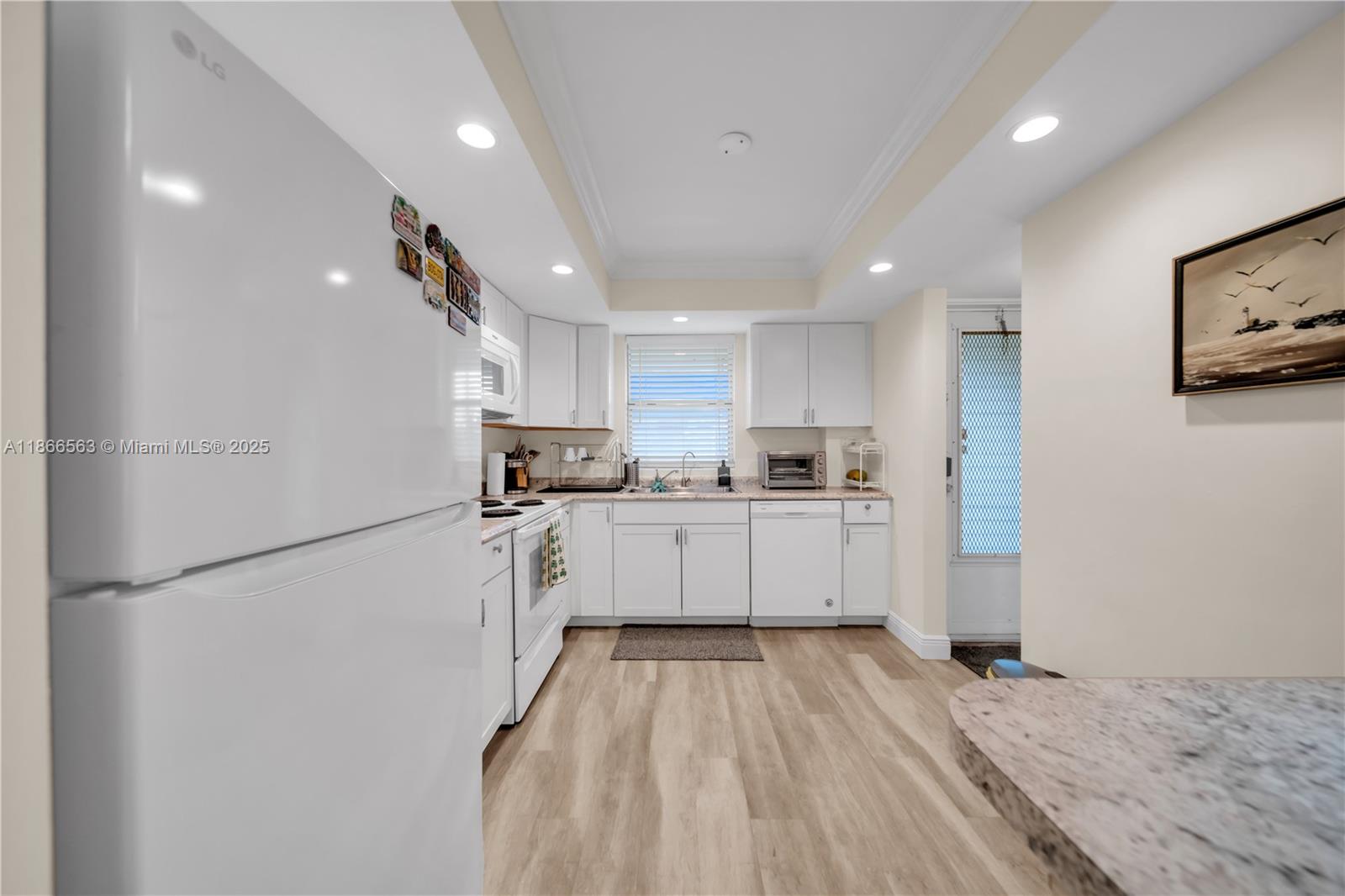 A white kitchen features light wood-look flooring, granite countertops, and a white refrigerator — 4613 SE 5th ave # 210, Cape Coral FL 33904, CAPE CORAL, FL