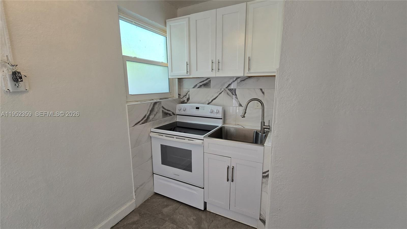 A small kitchen features white cabinets, a white stove, a sink, and marble-patterned backsplash tiles — 9680 NW 19th Pl, Sunrise FL 33322, SUNRISE, FL