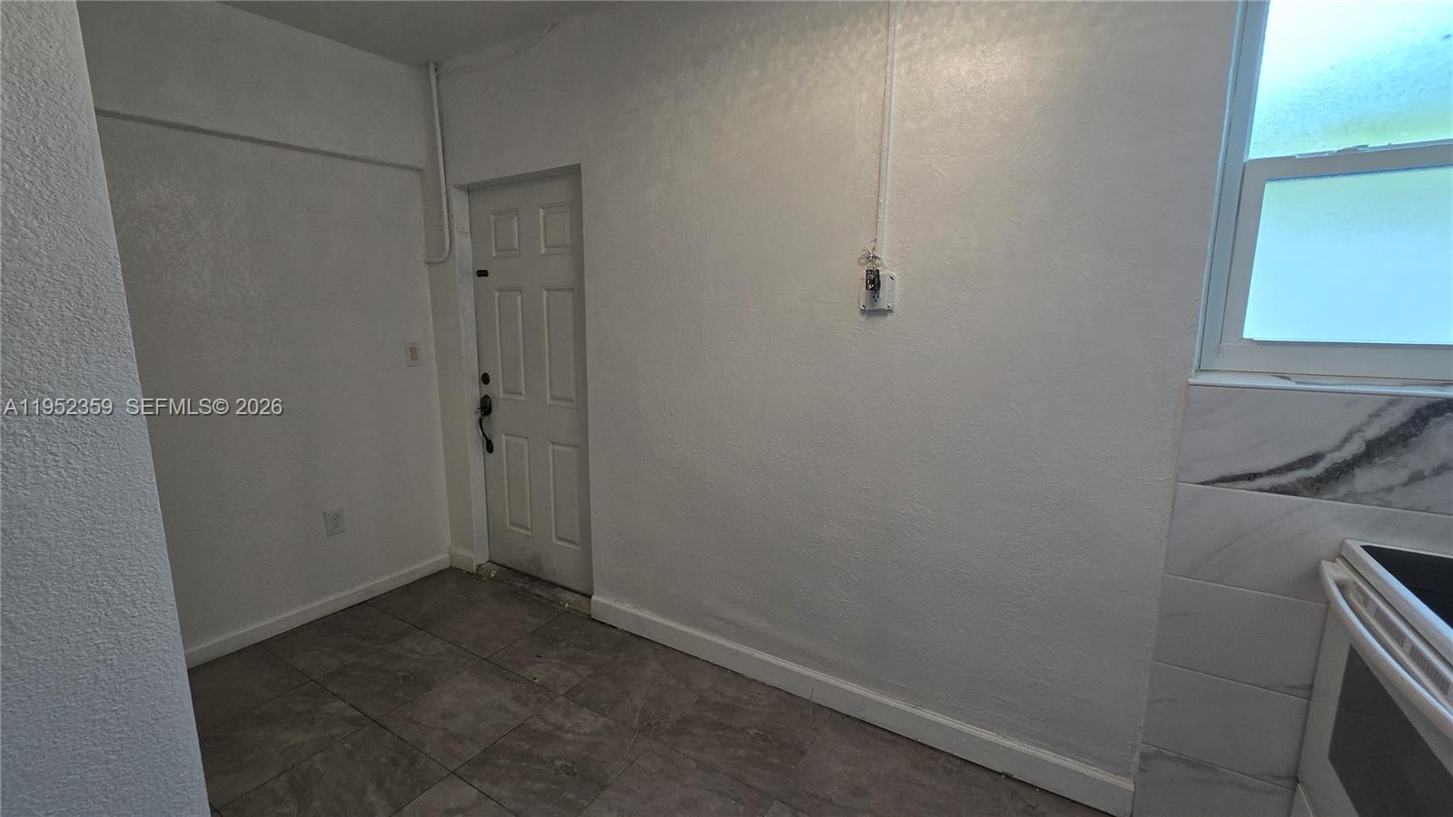 A kitchen area features white walls, tiled flooring, a white door, and a window — 9680 NW 19th Pl, Sunrise FL 33322, SUNRISE, FL