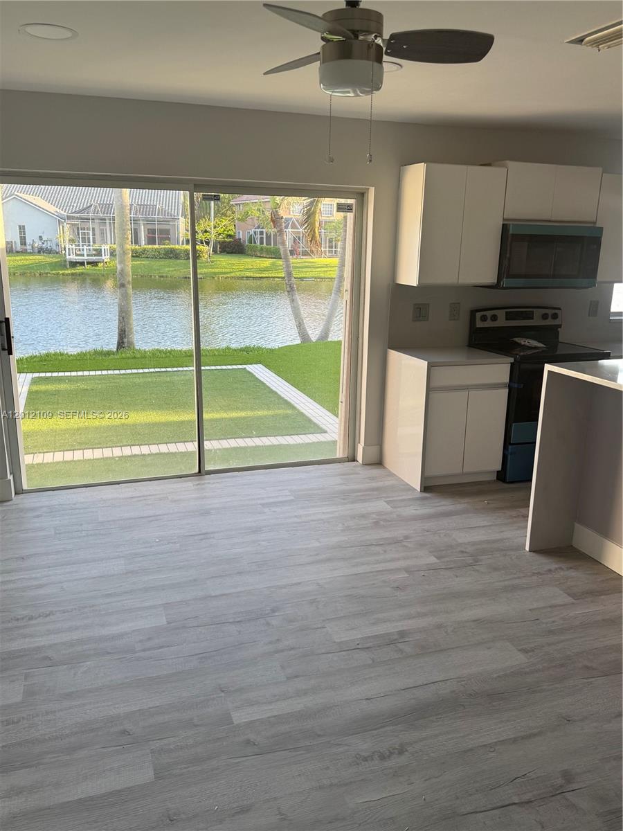 A kitchen with white cabinets and light wood flooring opens to a patio and lake — 13950 Oak Ridge Dr, Davie FL 33325, DAVIE, FL