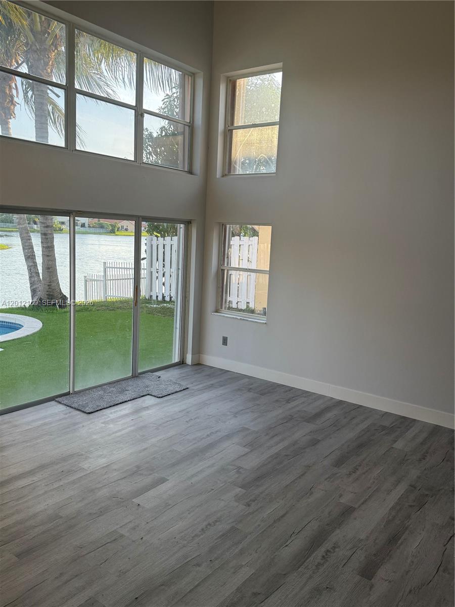 A room with gray wood-look flooring, high ceilings, and large windows overlooking a lake — 13950 Oak Ridge Dr, Davie FL 33325, DAVIE, FL