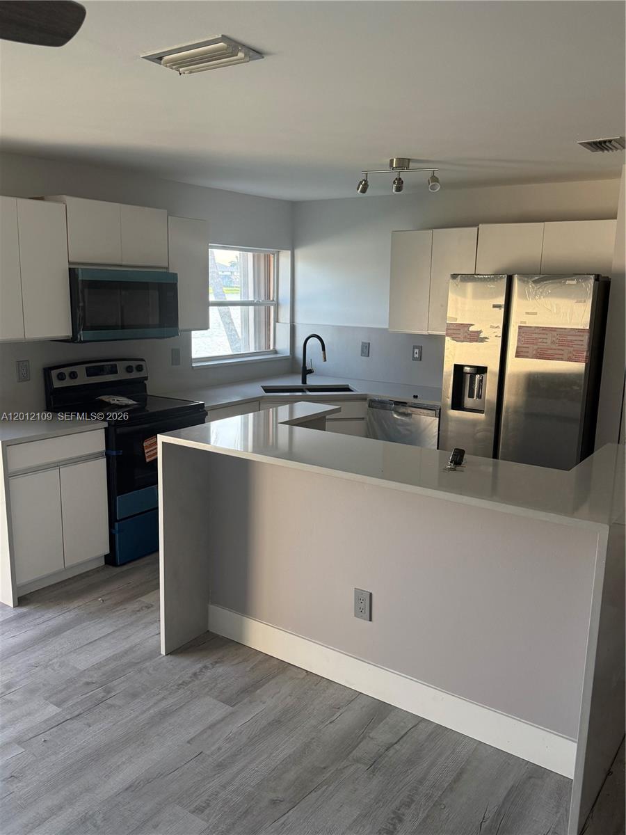 A modern kitchen features white cabinets, stainless steel appliances, and a white quartz peninsula — 13950 Oak Ridge Dr, Davie FL 33325, DAVIE, FL