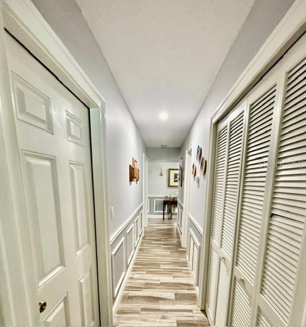 A hallway with light-colored walls, wood-look flooring, a white door, and louvered closet doors — 15116 ROUNDUP DRIVE, TAMPA, FL