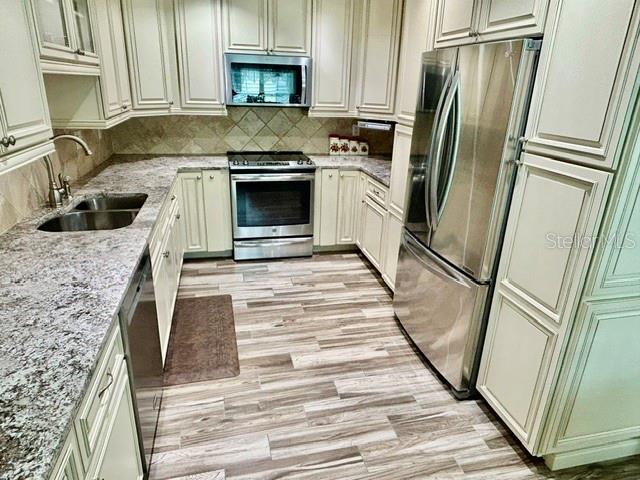 A kitchen features white cabinets, stainless steel appliances, and granite countertops over wood-look flooring — 15116 ROUNDUP DRIVE, TAMPA, FL