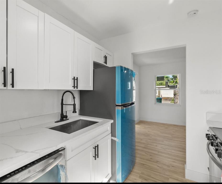A kitchen features white cabinets, a stainless steel sink, and a blue-wrapped refrigerator — 2352 EDNOR STREET, PORT CHARLOTTE, FL