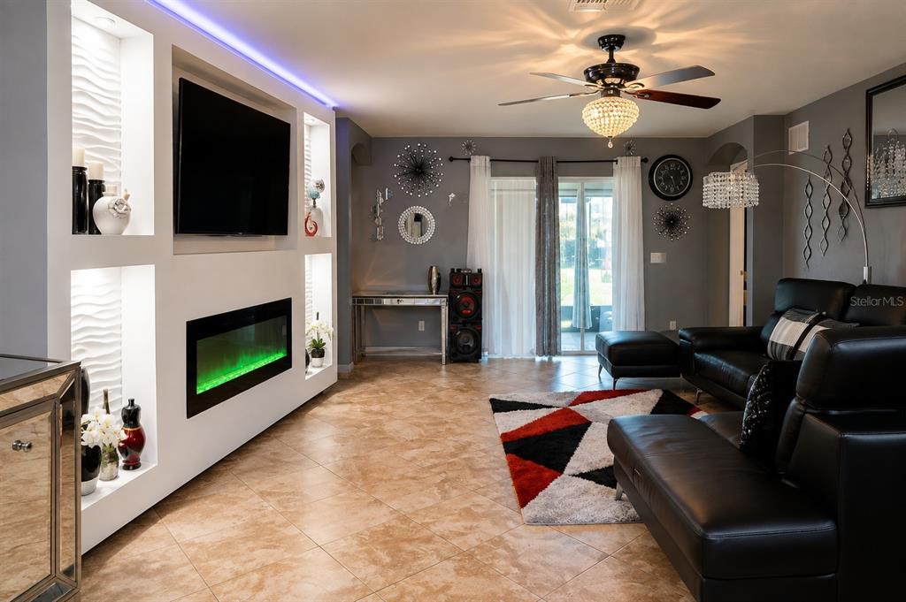 A living room features a built-in fireplace, a wall-mounted television, black leather furniture, and tile flooring — 413 SIERRA MIKE BOULEVARD, LAKE ALFRED, FL