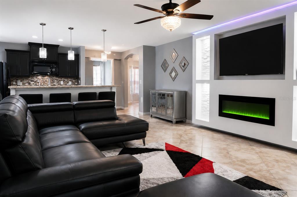 A living room with a black sectional sofa, fireplace, wall-mounted television, and an adjacent kitchen — 413 SIERRA MIKE BOULEVARD, LAKE ALFRED, FL