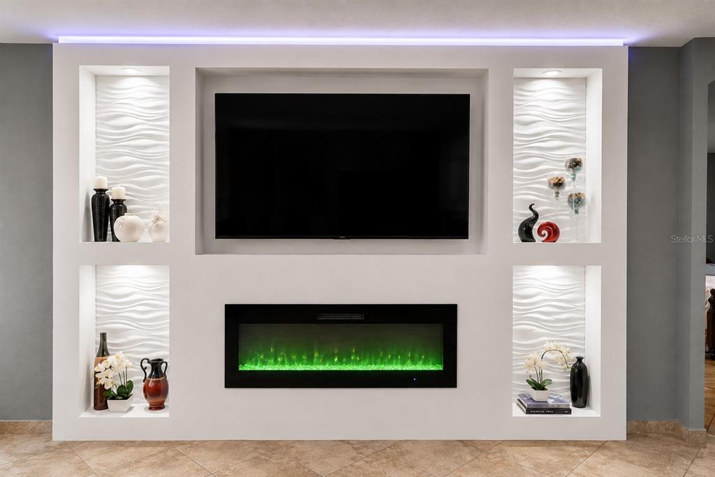 A white built-in wall unit features a television, electric fireplace, and illuminated decorative alcoves — 413 SIERRA MIKE BOULEVARD, LAKE ALFRED, FL