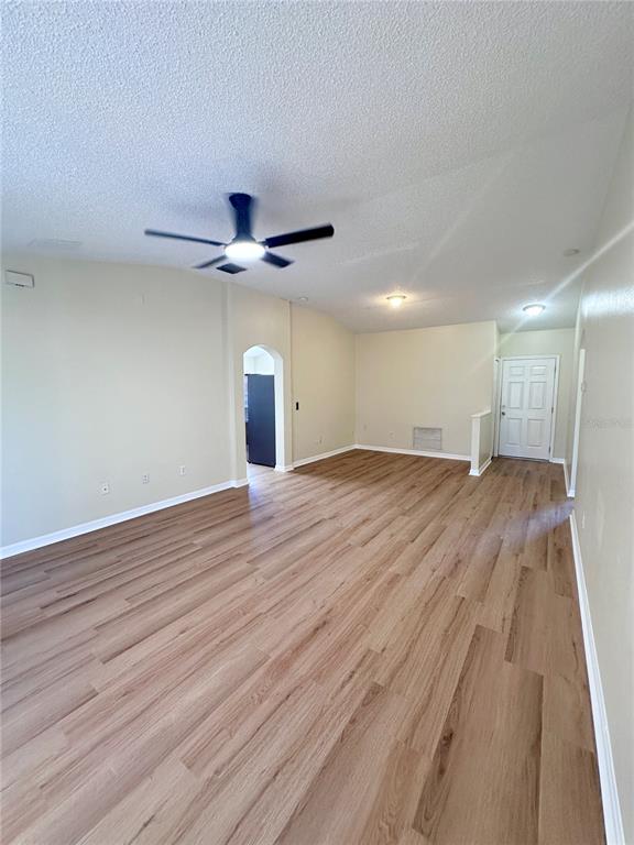 An empty living room features light wood-look flooring, a ceiling fan, and an arched doorway — 11030 WHITTNEY CHASE DRIVE, RIVERVIEW, FL