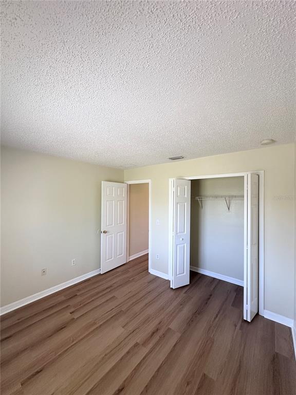 A bedroom with light-colored walls, wood-look flooring, a white door, and an open closet — 11030 WHITTNEY CHASE DRIVE, RIVERVIEW, FL
