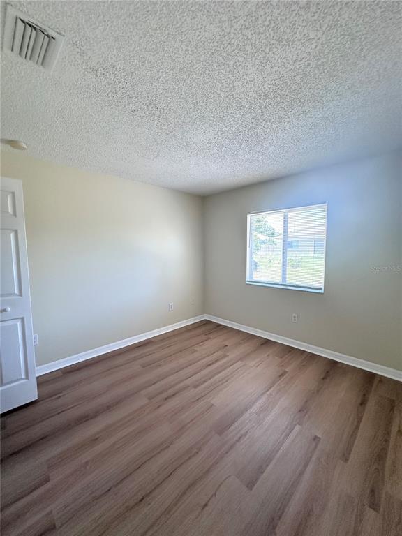 An empty bedroom features light-colored walls, wood-look flooring, a window, and a white door — 11030 WHITTNEY CHASE DRIVE, RIVERVIEW, FL